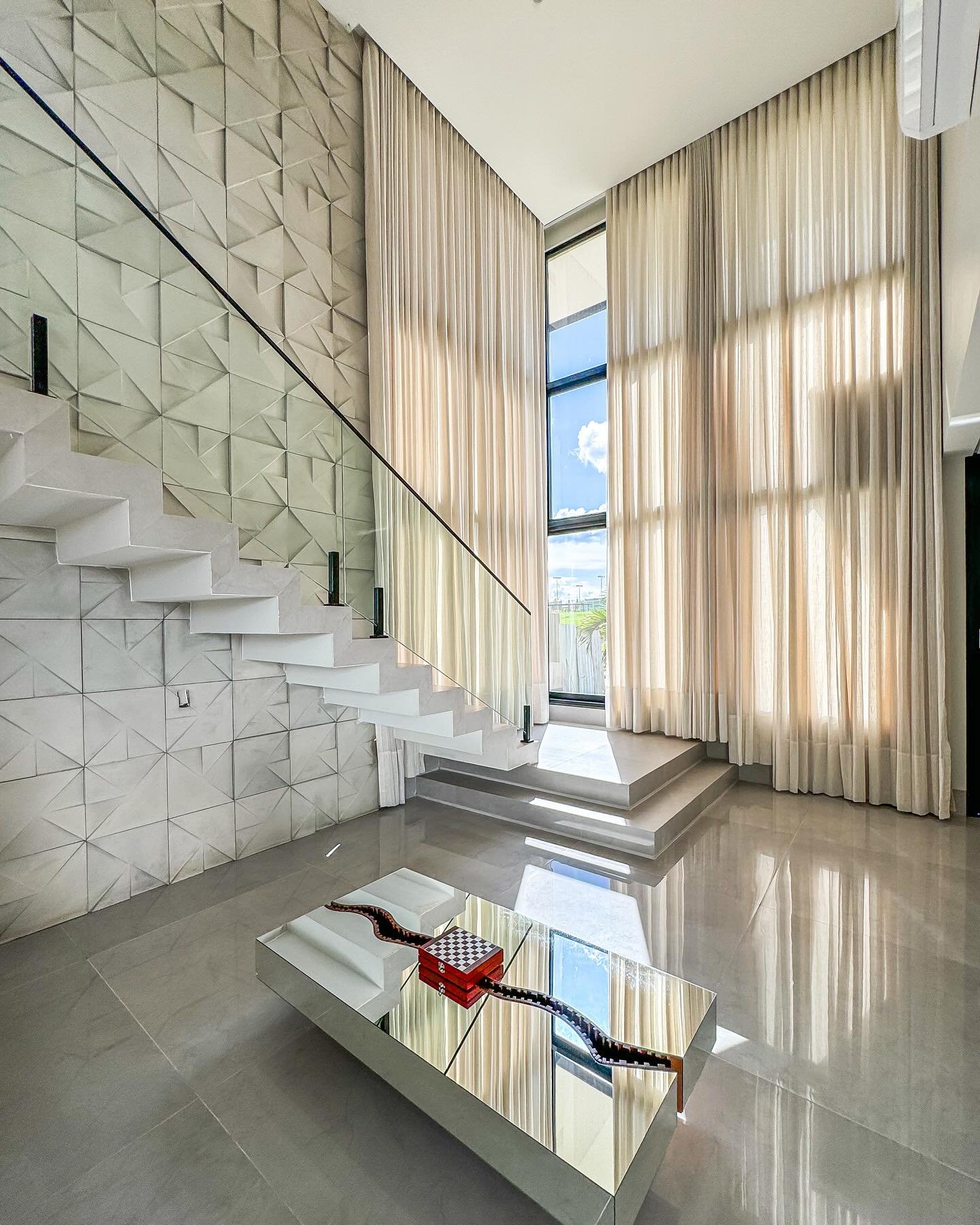Hall com cortinas de pé-direito duplo e escada escultural — projeto Arte House em Rio Verde, GO